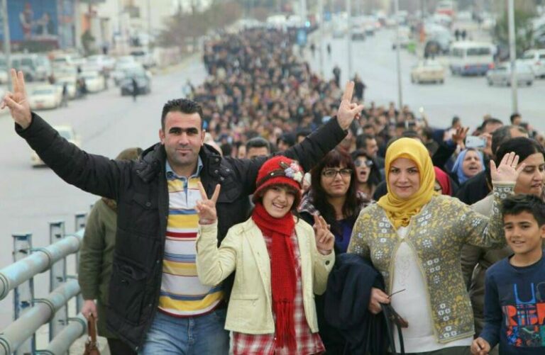 Una familia está de pie con los brazos en el aire, liderando a una multitud de cientos que llenan la calle detrás de ellos en la lejanía.