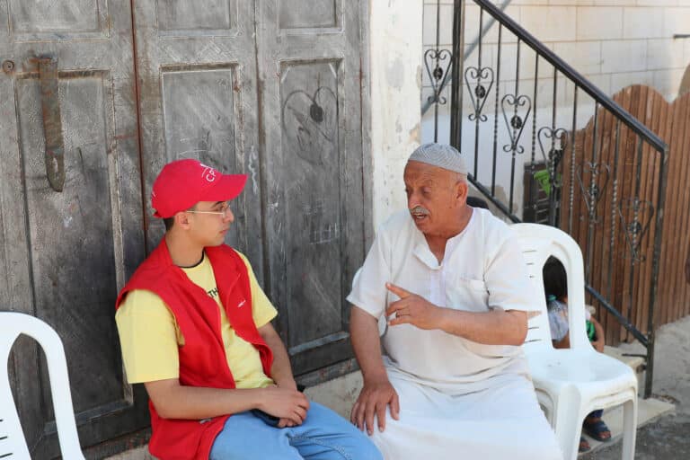 Miembro de ECAP con sombrero rojo escucha a un hombre con camisa blanca hablarle, sentados uno frente al otro.