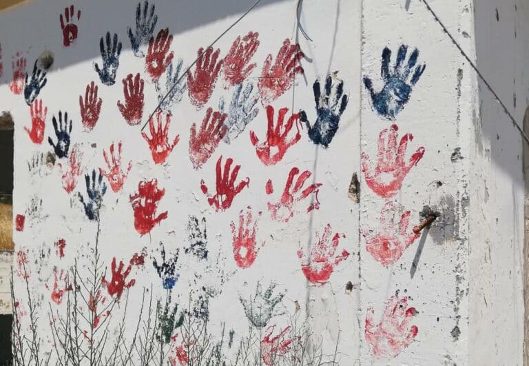 las huellas de las manos de los y las migrantes en pintura roja y azul cubren una pared blanca