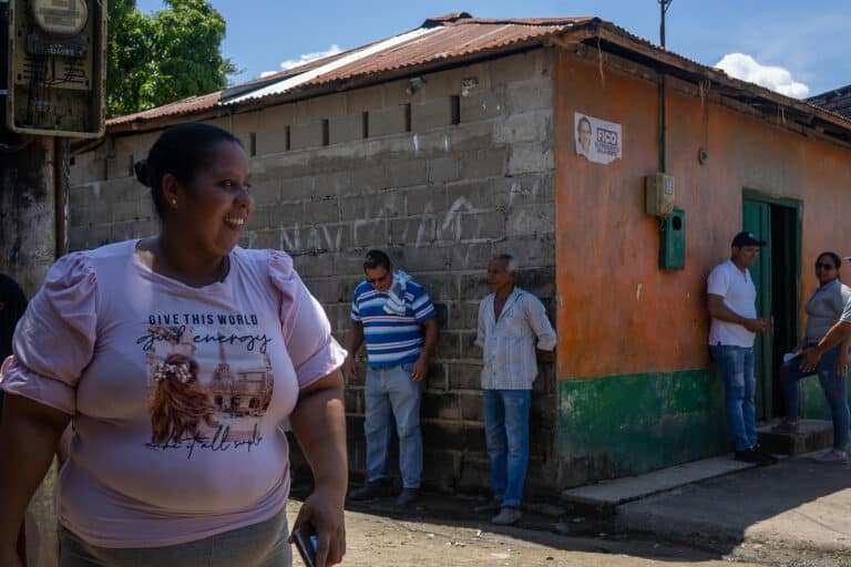 A woman walks in front of a house with people in the background