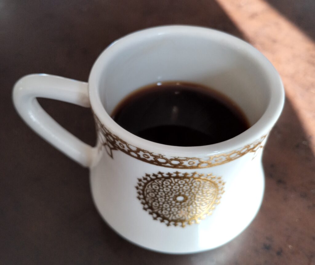 una taza de café de cerámica blanca con diseños dorados llena de café