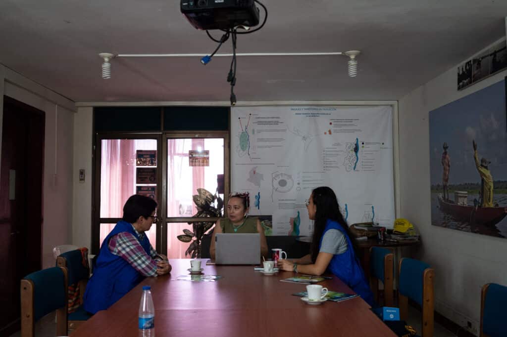 Three people sit around a meeting table in conversation.