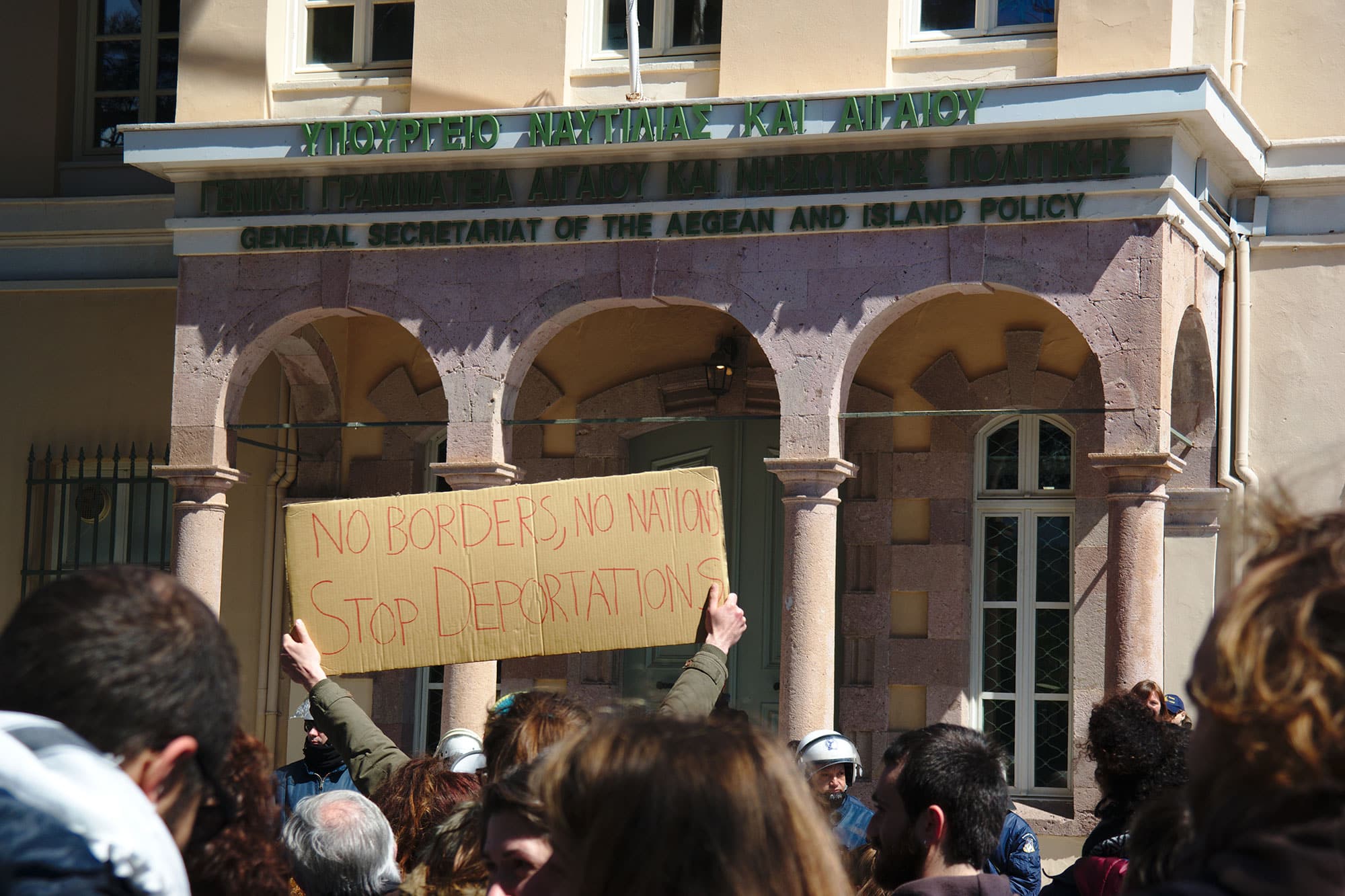 A view of a crowd from behind in front of a courthouse. A man holds a sign.