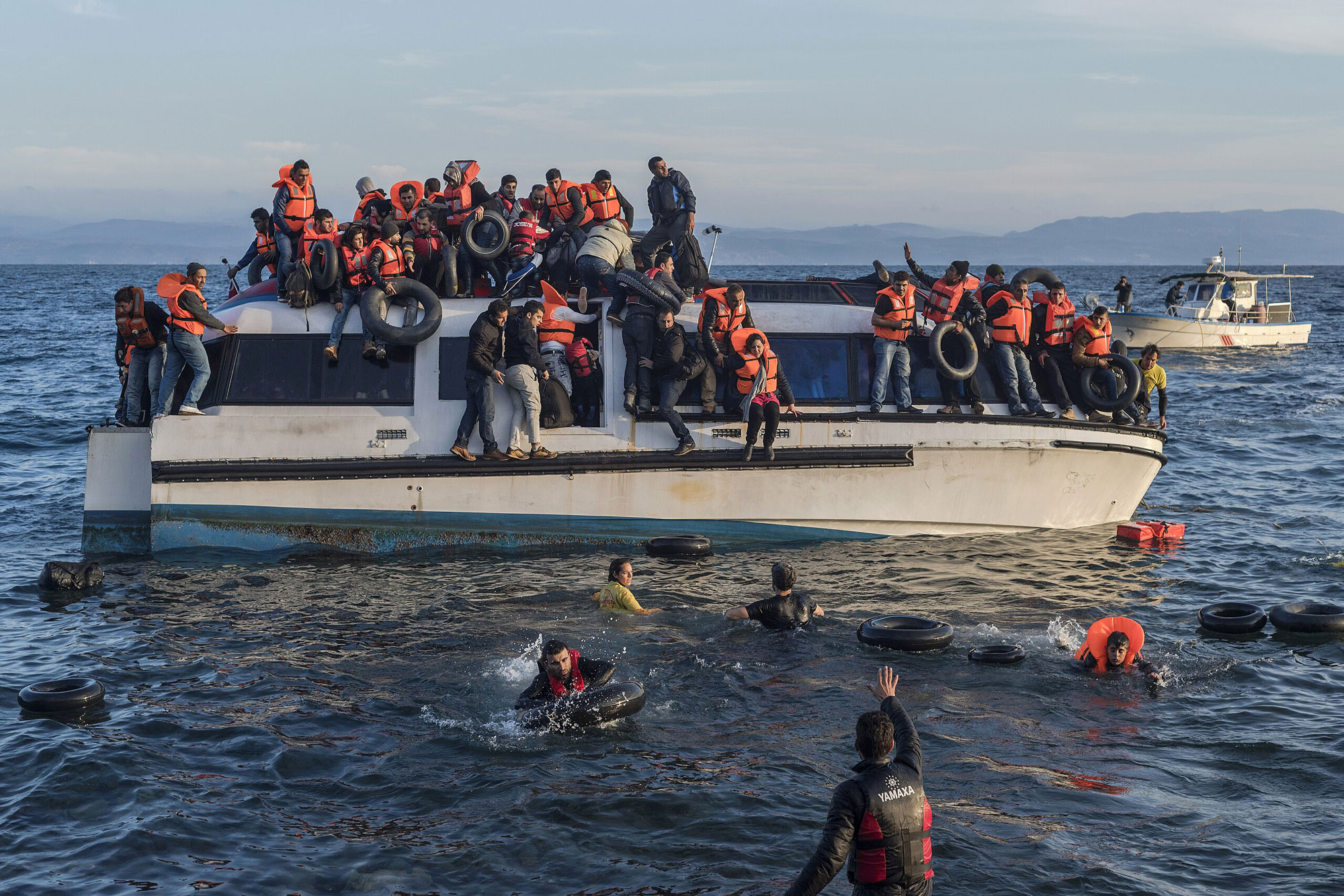 migrants wearing orange life jackets disembark off a boat in the aegean sea