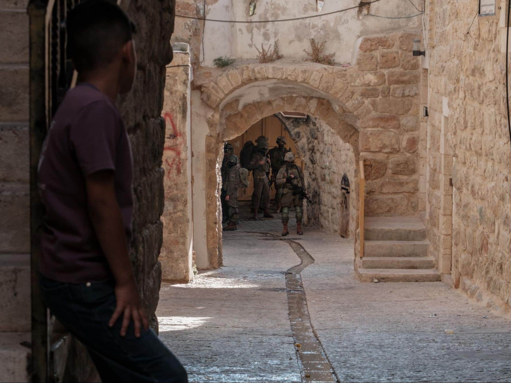 A boy looks down an old alleyway at a group of soldiers
