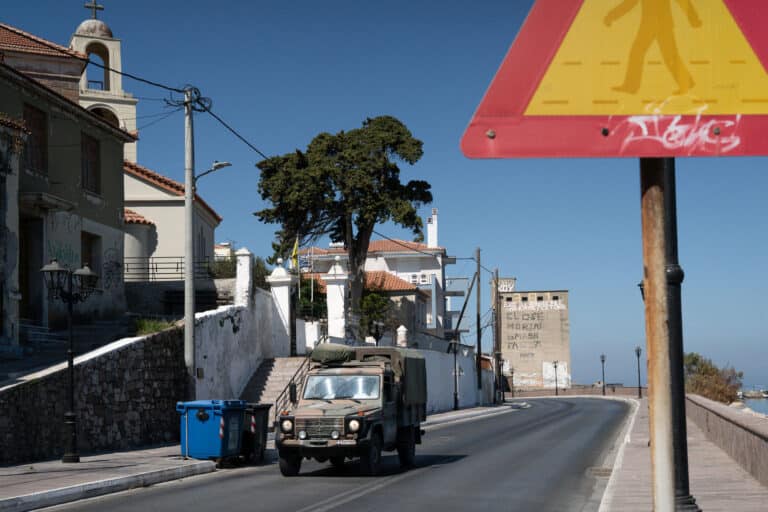 a greek military vehicle passes a wall with grafitti that reads close moria