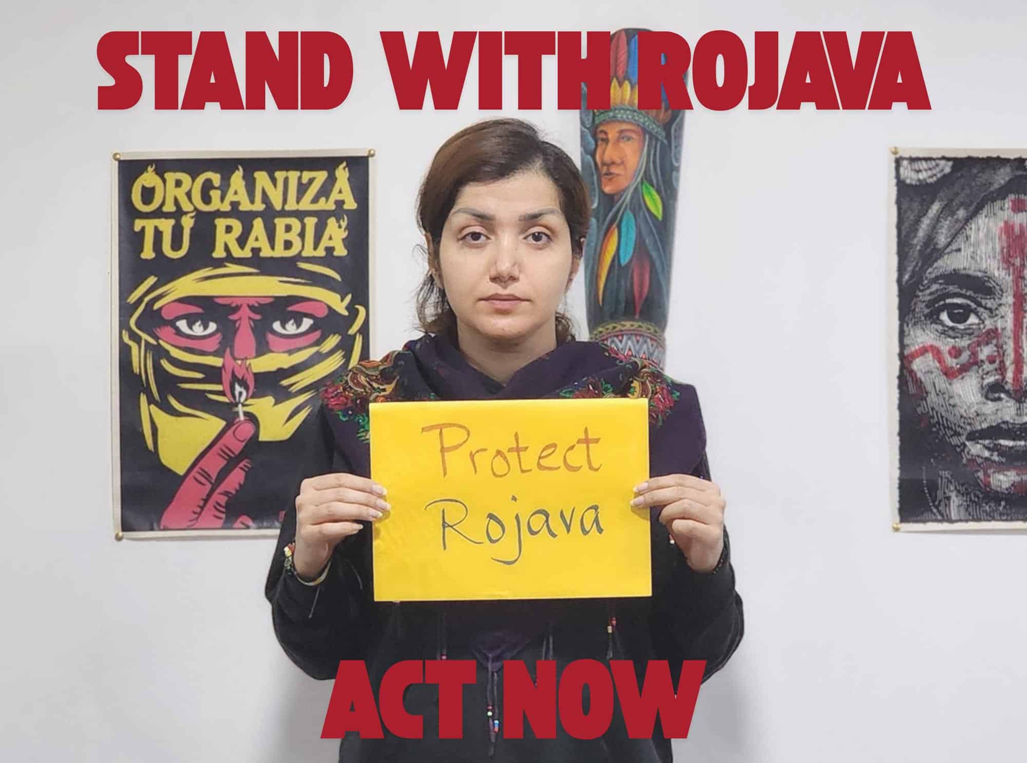 person holding sign that reads protect rojava