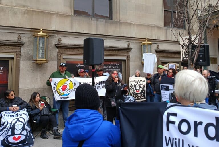 a woman speaks at a protest where people hold signs