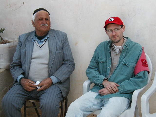 Two men sit on chairs and pose for a portrait