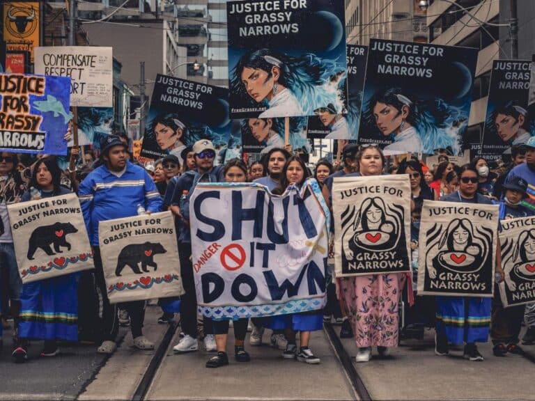 Image of the Grassy Nations community members leading the River Run march in 2024. Signs read “Shut it down”, and “Justice for Grassy Narrows.”