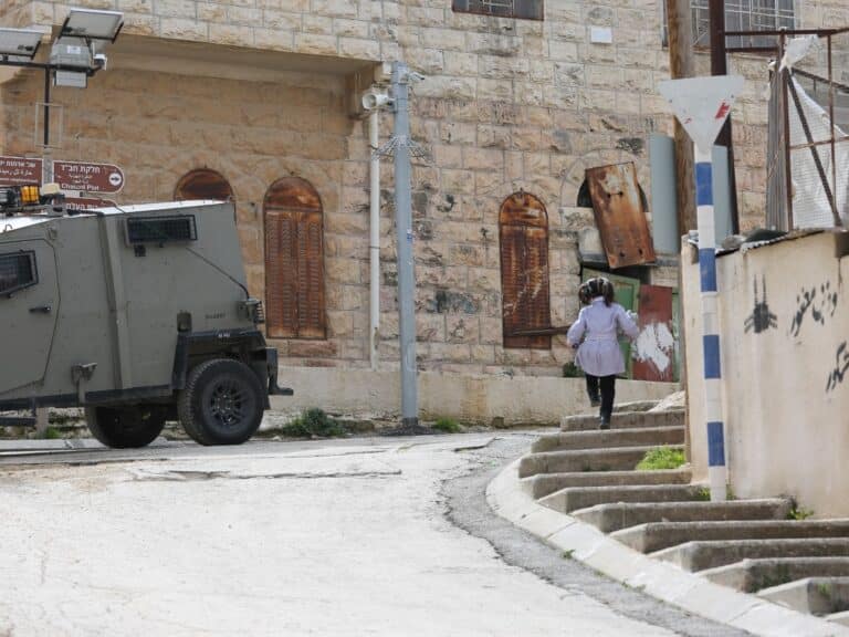 A child walking along the road past a military vehicle