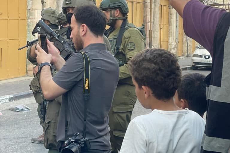 A man standing next to soldiers takes a photo on his phone